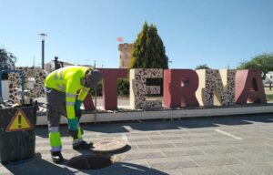 Trabajador limpiando un embornal en Paterna con letras grandes de fondo