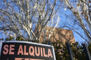 Cartel de se alquila en una vivienda con árboles al fondo