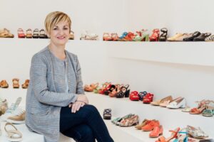 Marián Cano en una tienda de calzado, rodeada de zapatos coloridos.