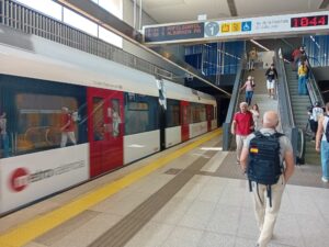 Estación de Metrovalencia con tren y pasajeros en movimiento