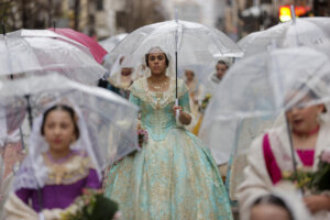 Varias falleras desfilan protegidas de la lluvia con paraguas durante la ofrenda de flores a la Virgen de los Desamparados.