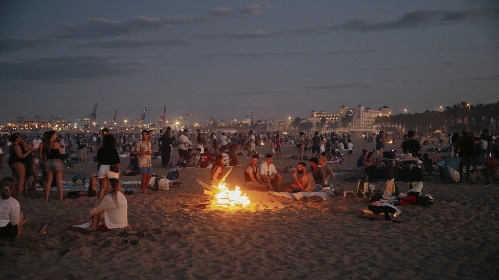 Celebración de la Nit de Sant Joan en la playa de Valencia con fogatas y gente disfrutando.