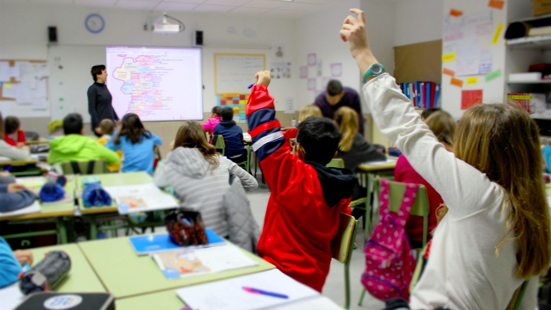 Alumnos en clase levantando la mano durante una lección interactiva.
