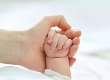 Mano de un adulto sosteniendo la mano de un bebé.