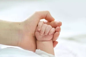 Mano de un adulto sosteniendo la mano de un bebé.