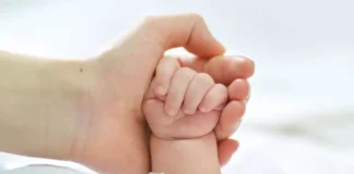 Mano de un adulto sosteniendo la mano de un bebé.