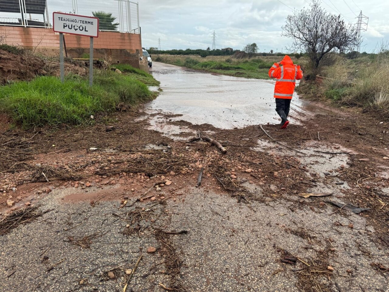 Persona con chaqueta naranja caminando por carretera afectada por inundaciones en Pucol