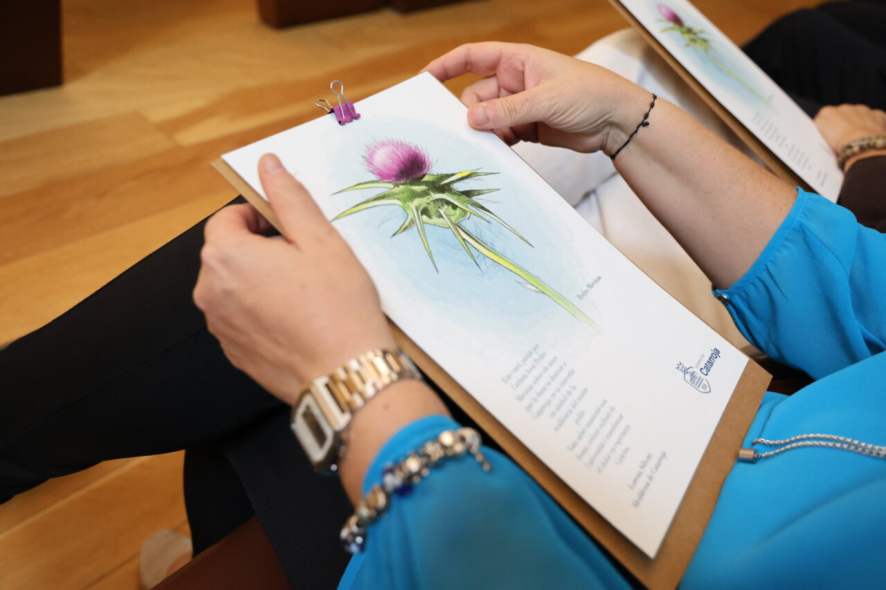 Persona sosteniendo un documento con un dibujo de un cardo en un acto de homenaje.