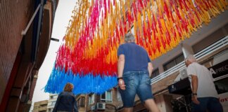 Decoraciones de la calle Sagra con lazos de colores rojo, amarillo y azul en Torrent.