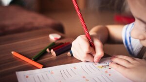 Un niño escribiendo en una hoja con lápices de colores alrededor.