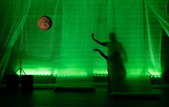 Actores en escena con fondo verde y luna llena en un espectáculo infantil.