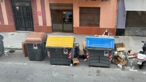 Contenedores de basura en una calle de València con residuos alrededor.