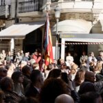 Ceremonia de homenaje con una multitud y una bandera en la plaza.