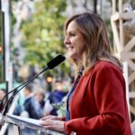 Mujer hablando en un evento con micrófono en mano y público al fondo