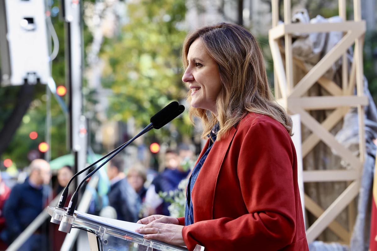 Mujer hablando en un evento con micrófono en mano y público al fondo
