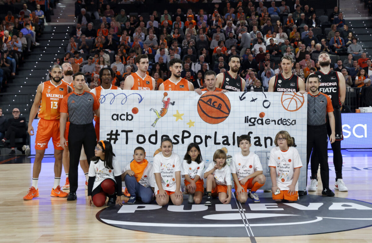 Jugadores de Valencia Basket y Girona posando con una pancarta en el Roig Arena.