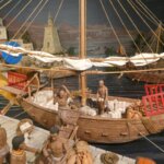 Modelo de barco antiguo con figuras humanas en actividad comercial.