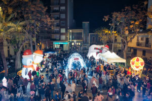 Calle iluminada con figuras gigantes y gente celebrando el inicio de Navidad