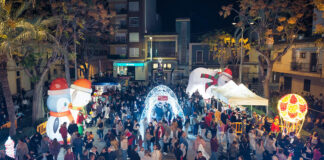 Calle iluminada con figuras gigantes y gente celebrando el inicio de Navidad