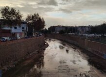 12 municipios de l'Horta cerrarán sus centros escolares mientras otros 21 los abrirán este lunes 15 por la alerta por lluvias Vista del cauce de un río seco en Massanassa con edificios al fondo.