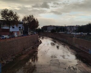 Vista del cauce de un río seco en Massanassa con edificios al fondo.