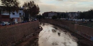 12 municipios de l'Horta cerrarán sus centros escolares mientras otros 21 los abrirán este lunes 15 por la alerta por lluvias Vista del cauce de un río seco en Massanassa con edificios al fondo.