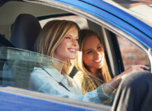 Dos jóvenes sonriendo dentro de un coche mientras conducen.