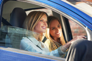 Dos jóvenes sonriendo dentro de un coche mientras conducen.
