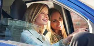 Dos jóvenes sonriendo dentro de un coche mientras conducen.