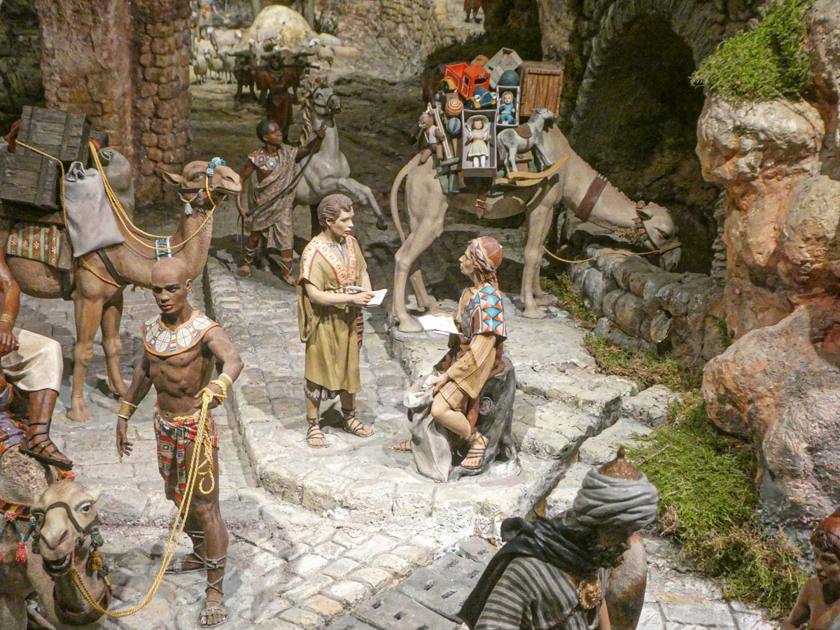 Escena de comercio antiguo con figuras y camellos en un entorno detallado.