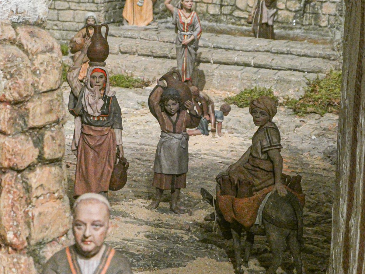 Figuras de personas en un entorno rural con jarras y un burro.