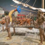 Escena histórica con esculturas de personas cargando un felino