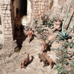 Escena de una calle con figuras humanas y perros en un paisaje rocoso.