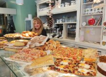 Mujer sonriente en una panadería con productos navideños variados.