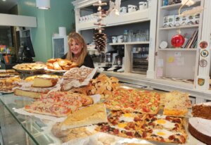 Mujer sonriente en una panadería con productos navideños variados.