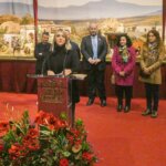 Una mujer habla en un evento navideño con decoraciones y público detrás.