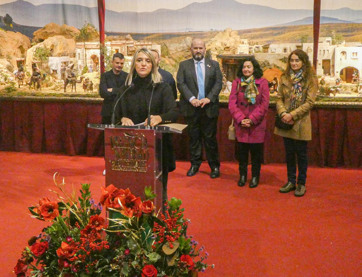 Una mujer habla en un evento navideño con decoraciones y público detrás.