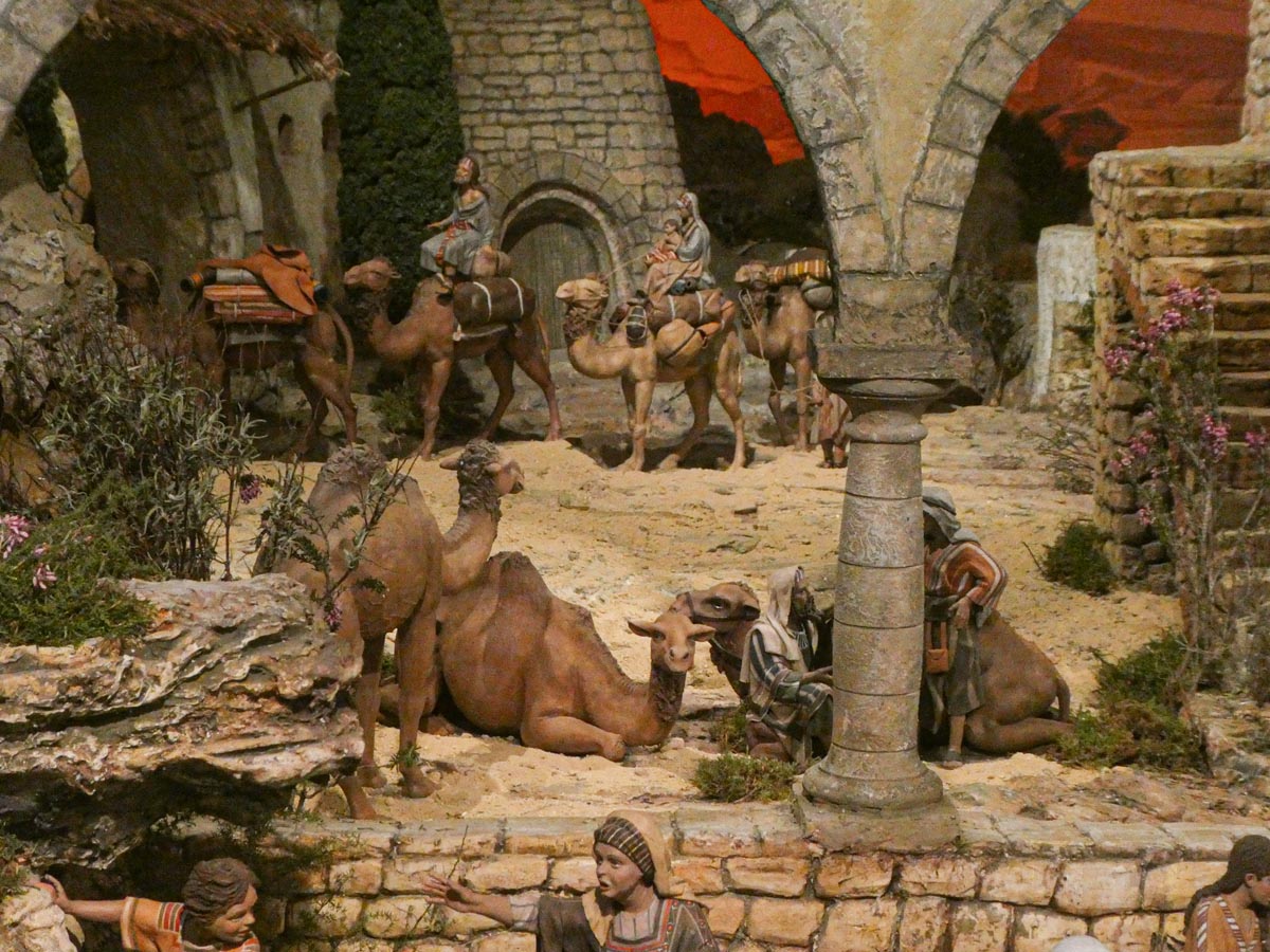 Escena de un nacimiento con camellos y pastores en un entorno rústico.