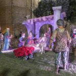 Escena de nacimiento con figuras de la Navidad y flores rojas.