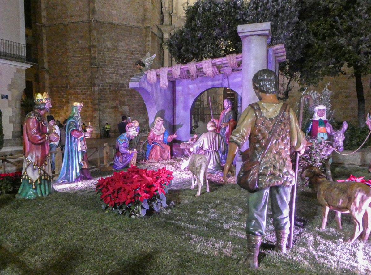 Escena de nacimiento con figuras de la Navidad y flores rojas.