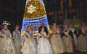 Grupo de personas vestidas con trajes tradicionales junto a un árbol de Navidad iluminado
