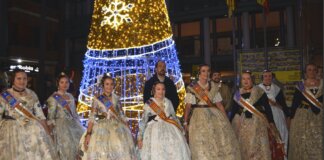 Grupo de personas vestidas con trajes tradicionales junto a un árbol de Navidad iluminado