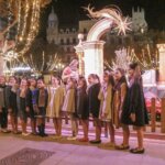 Grupo de niñas posando en una plaza iluminada por luces navideñas.