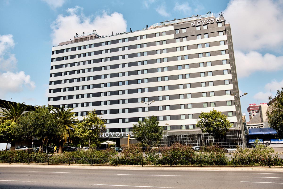 Fachada del hotel Novotel Valencia con vegetación y cielo azul