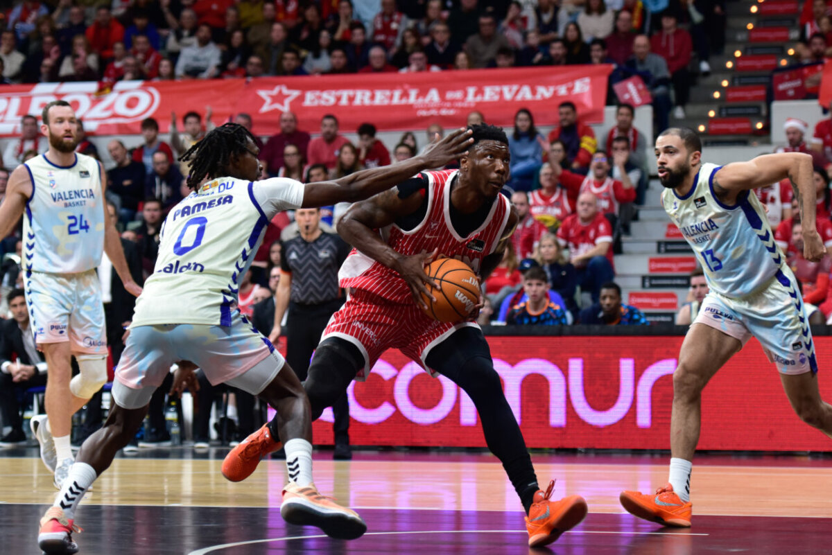 Jugadores de UCAM Murcia y Valencia Basket compiten por el balón en un partido de baloncesto.