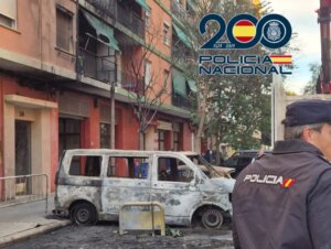 Policía en Valencia junto a un vehículo quemado y contenedores dañados