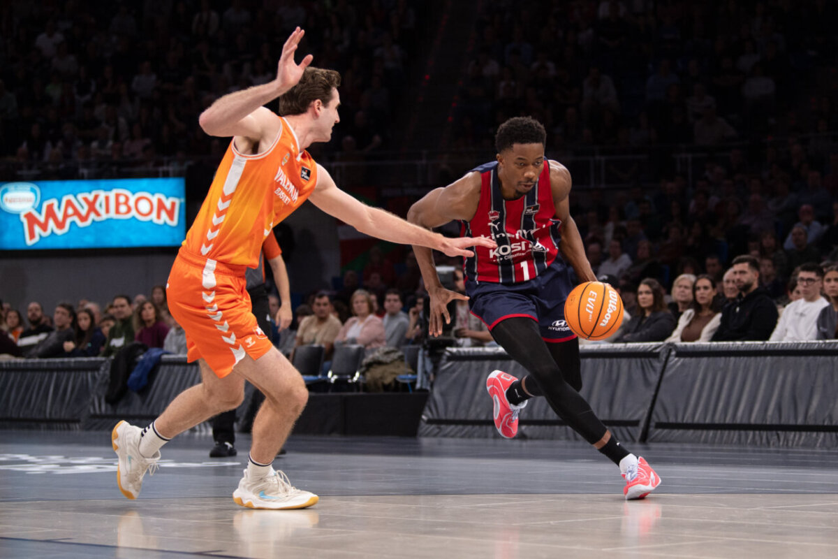 Jugador de Valencia Basket persigue a un rival del Baskonia en un partido emocionante.