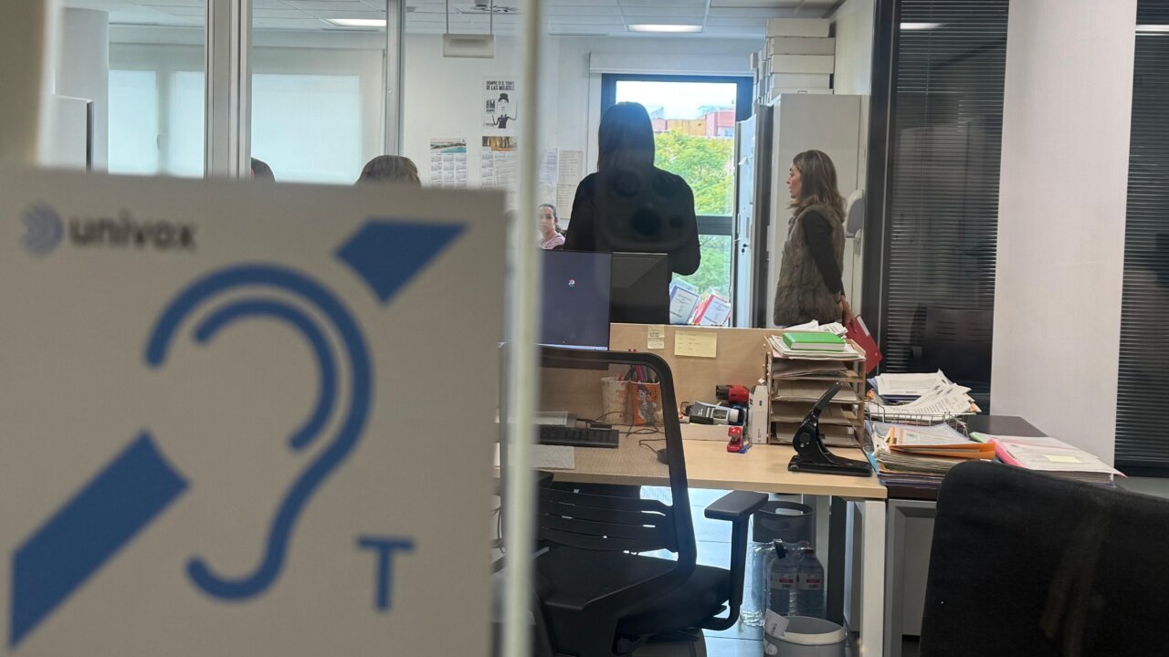 Vista de una oficina con personas conversando y un cartel de accesibilidad auditiva.