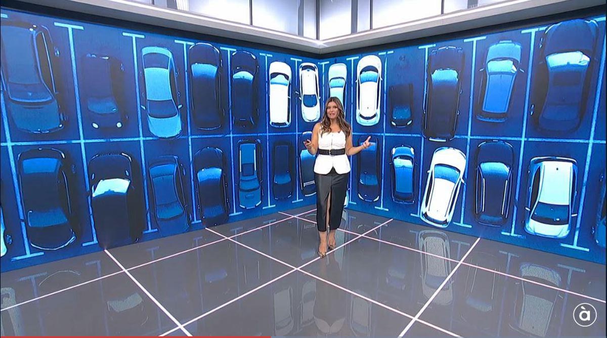 Presentadora en un set de televisión con fondo de coches À Punt