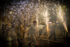 Participantes en la Entrà de la Flor con ramas de almendro en flor y fuegos artificiales.